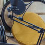 Podcast Affiliates - Modern laptop and microphone on tripod placed near wicker chair in modern studio before recording podcast