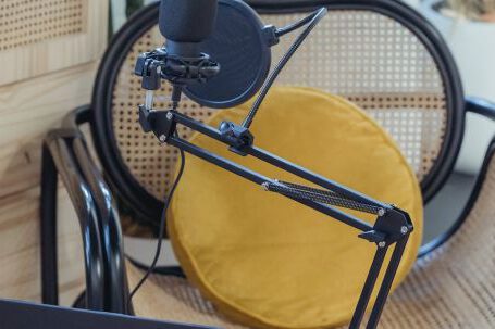Podcast Affiliates - Modern laptop and microphone on tripod placed near wicker chair in modern studio before recording podcast
