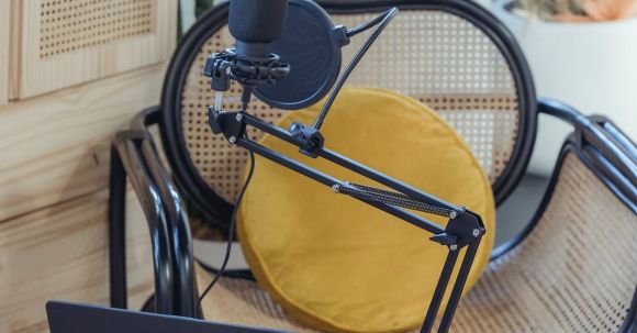 Podcast Affiliates - Modern laptop and microphone on tripod placed near wicker chair in modern studio before recording podcast
